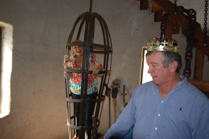 A visitor to the castle indulges the king's humor and occupies the hanging cage in the castle's dungeon.